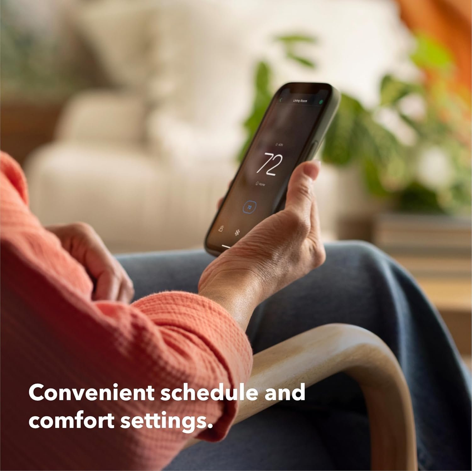 A person sitting comfortably in a chair and using the Ecobee app on a smartphone to adjust schedule and comfort settings.