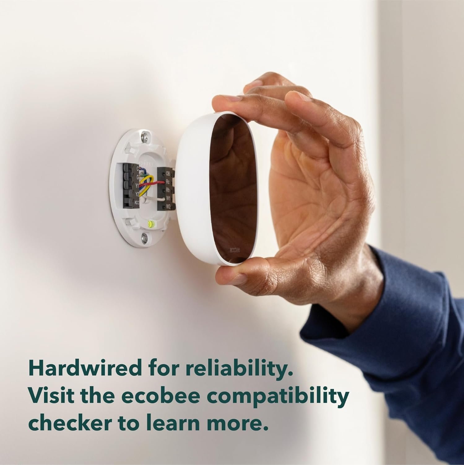 A person's hand installing the Ecobee thermostat onto its wall-mounted backplate, showing the "Hardwired for reliability" feature.