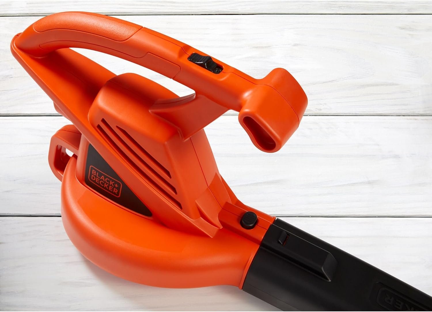 A close-up studio shot of the ergonomic handle and power switch on the BLACK+DECKER leaf blower, resting on a white painted wood surface.